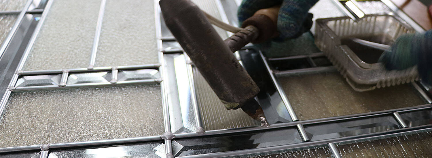 The joints of a bevelled glass panel being soldered