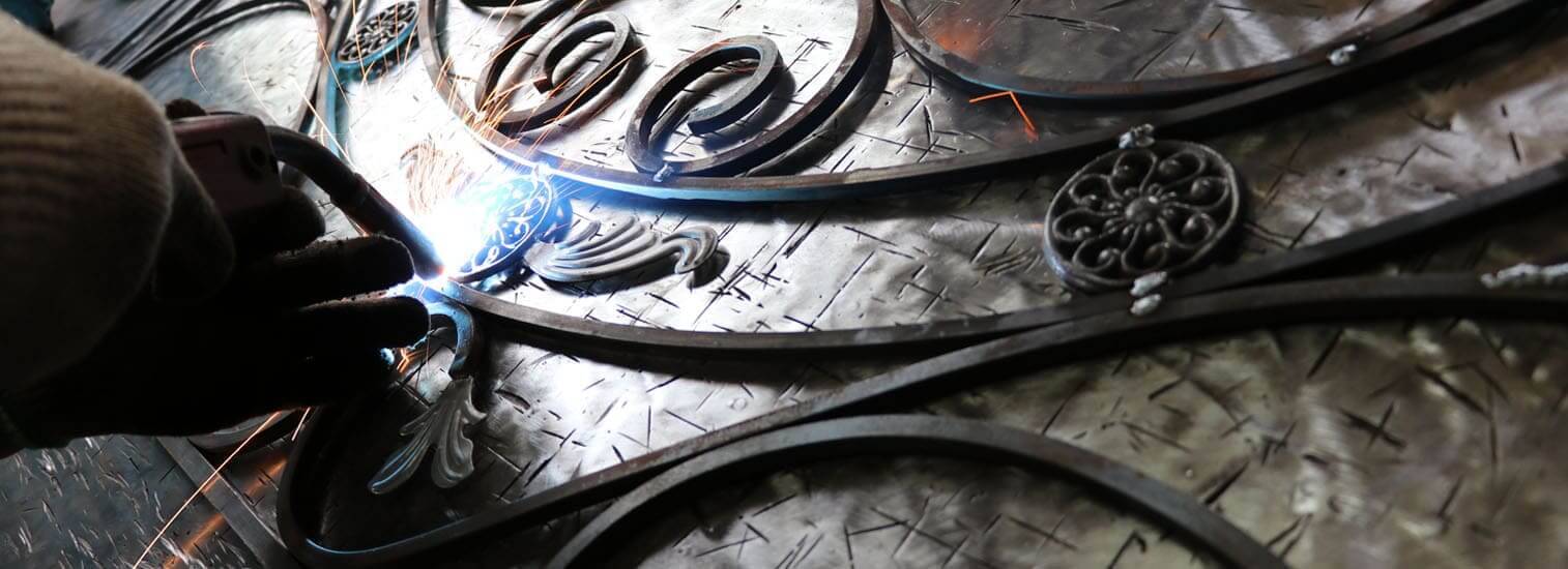 A scroll being welded onto a wrought iron panel