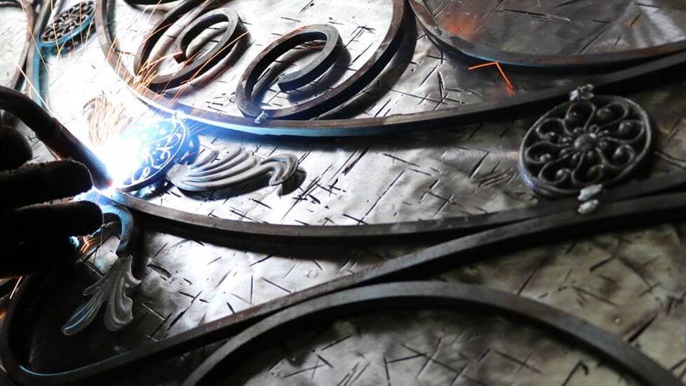 A scroll being welded onto a wrought iron panel
