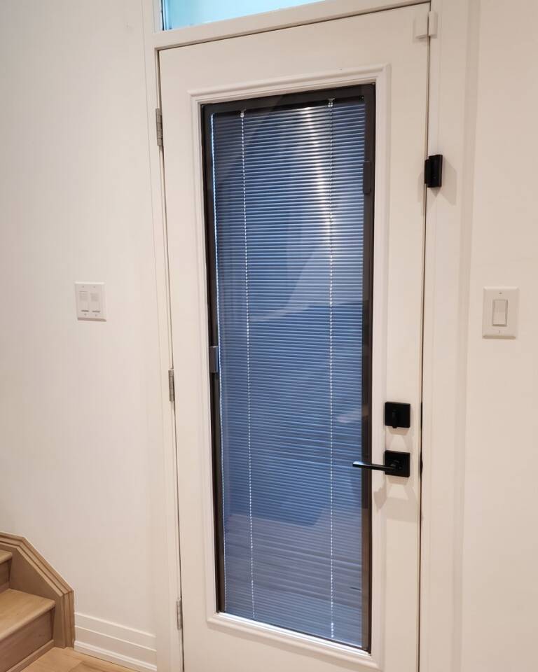 A single door with grey blinds between the glass and a transom above