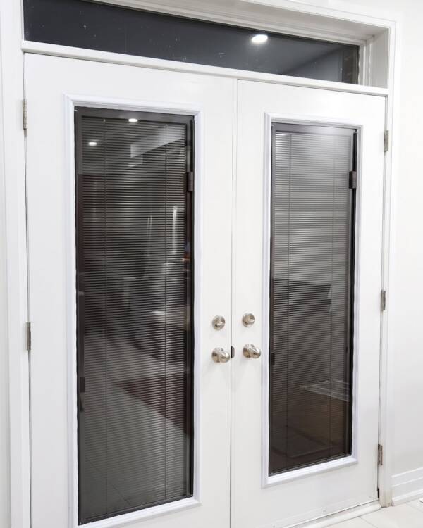 A white double door with brown blinds and a transom
