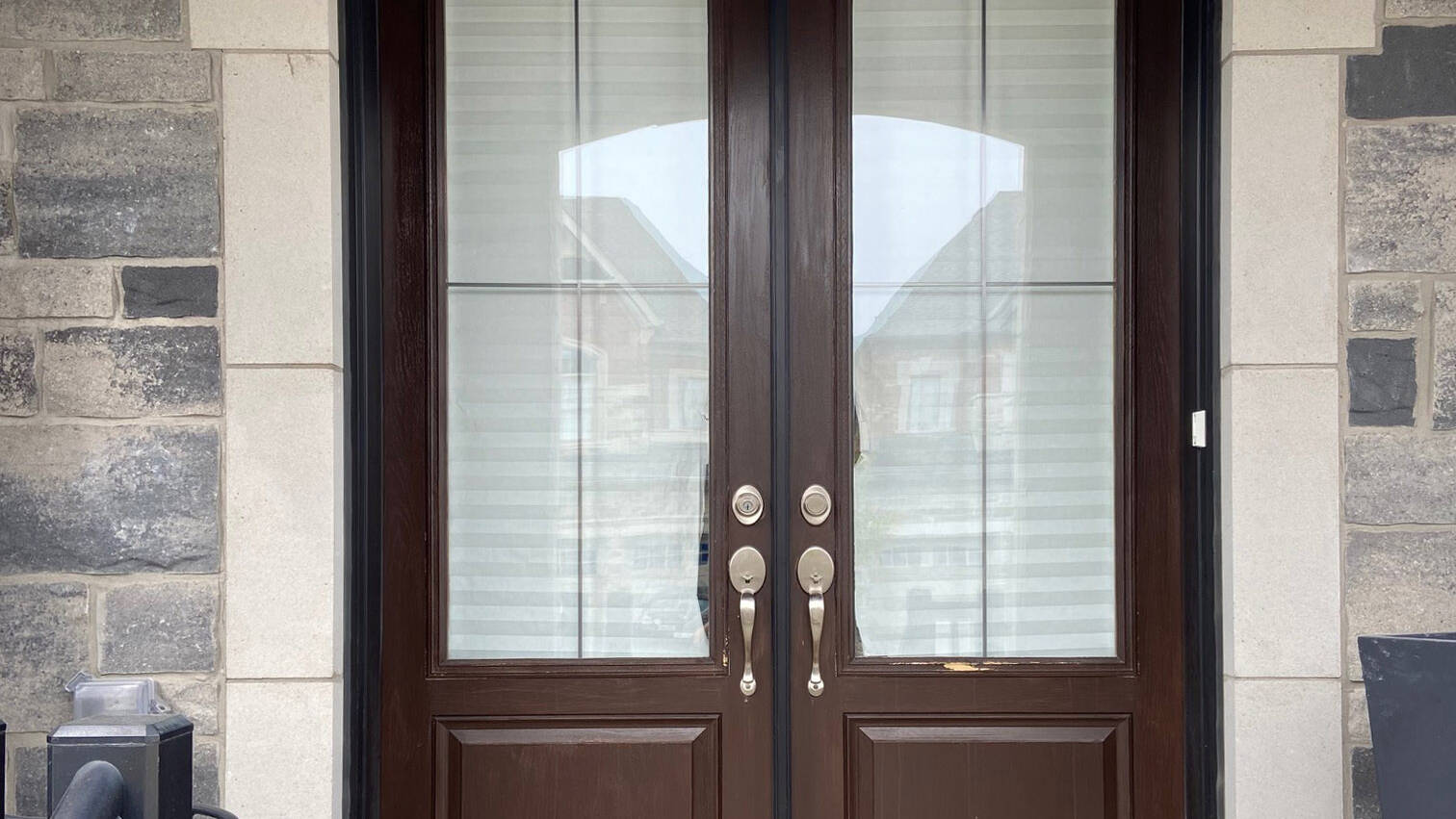 A brown double front door with plain glass, in a stone entrance